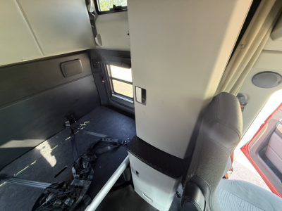 Truck cab interior showing sleeper area with seat and partition, door window in background and loose strap on floor.