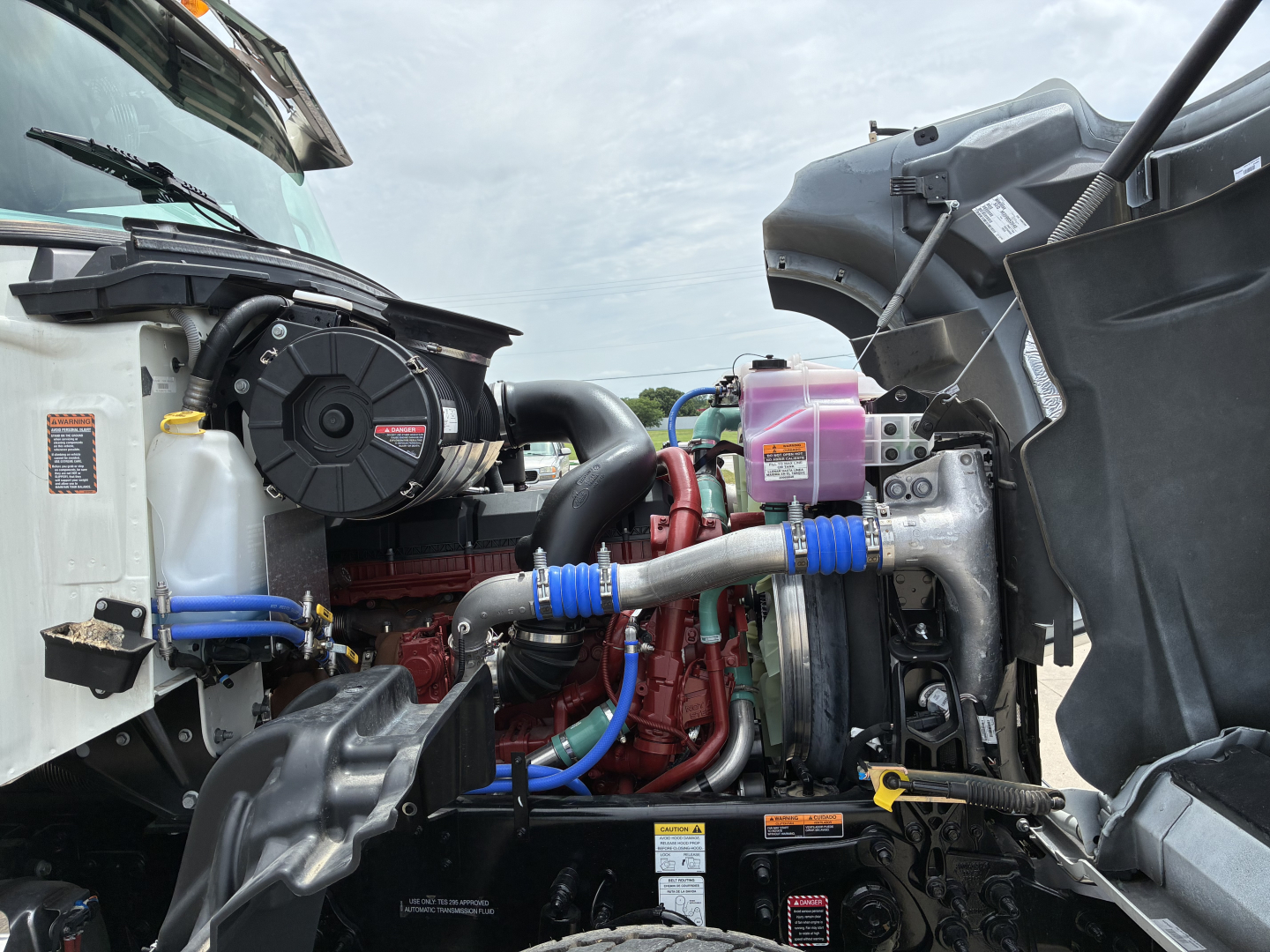 Mack GR64F engine bay showing components and fluid reservoirs under hood.