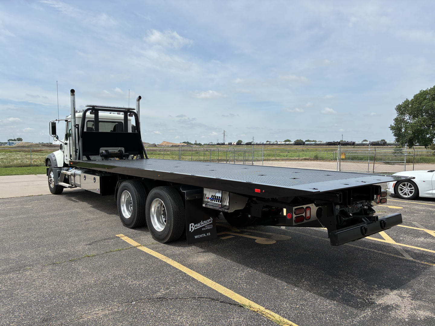 Flatbed tow truck with long steel deck and dual rear axles, Mack GR64F, showing heavy-duty towing platform and rear lights.