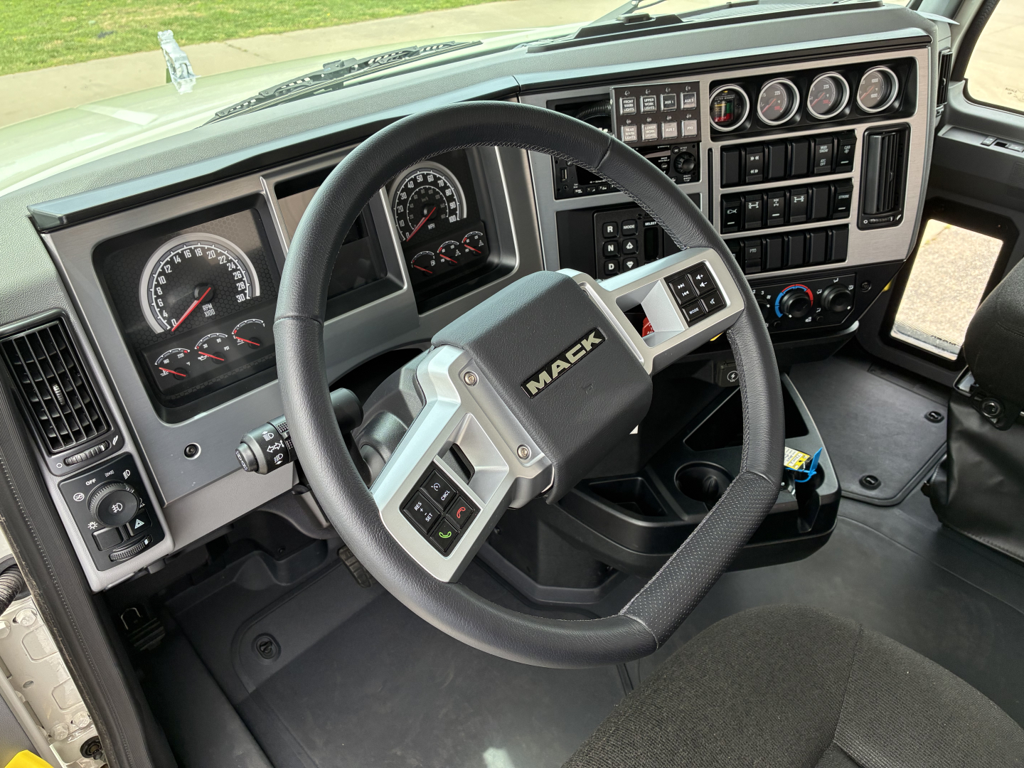 Mack GR64F truck interior showing steering wheel with Mack logo, instrument cluster, and control panel with numerous gauges and switches.