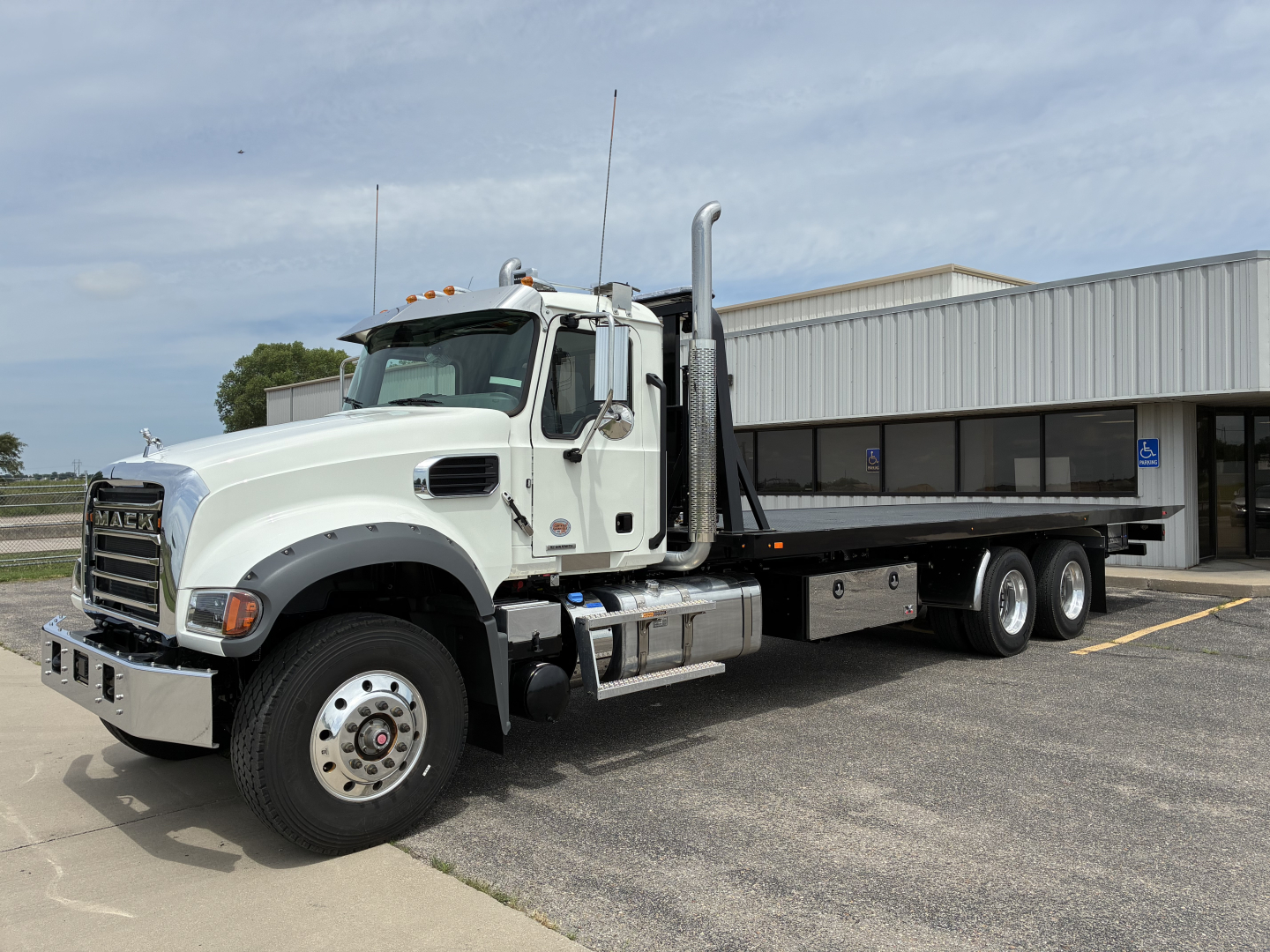 Mack GR64F rollback truck in white showing cab and flatbed with dual rear axles, front grille, chrome bumper, and exhaust stack.