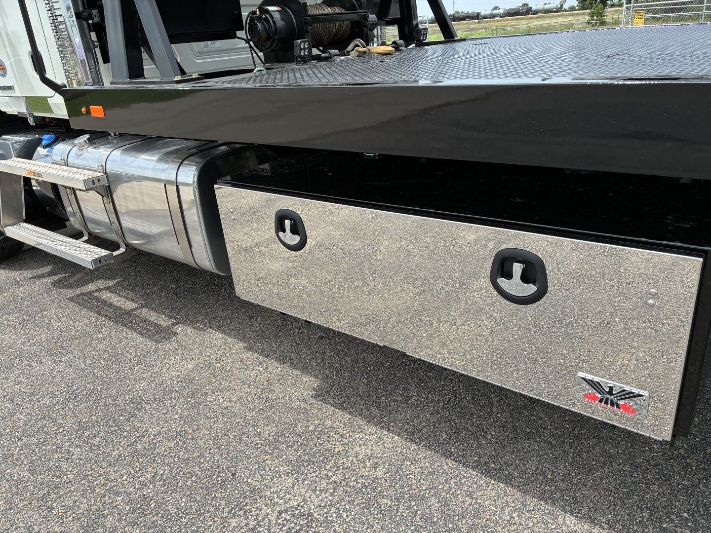 Mack GR64F rollback truck side view showing aluminum tool/storage box with two recessed handles and Mack logo.