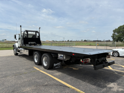 Flatbed tow truck with long steel deck and dual rear axles, Mack GR64F, showing heavy-duty towing platform and rear lights.