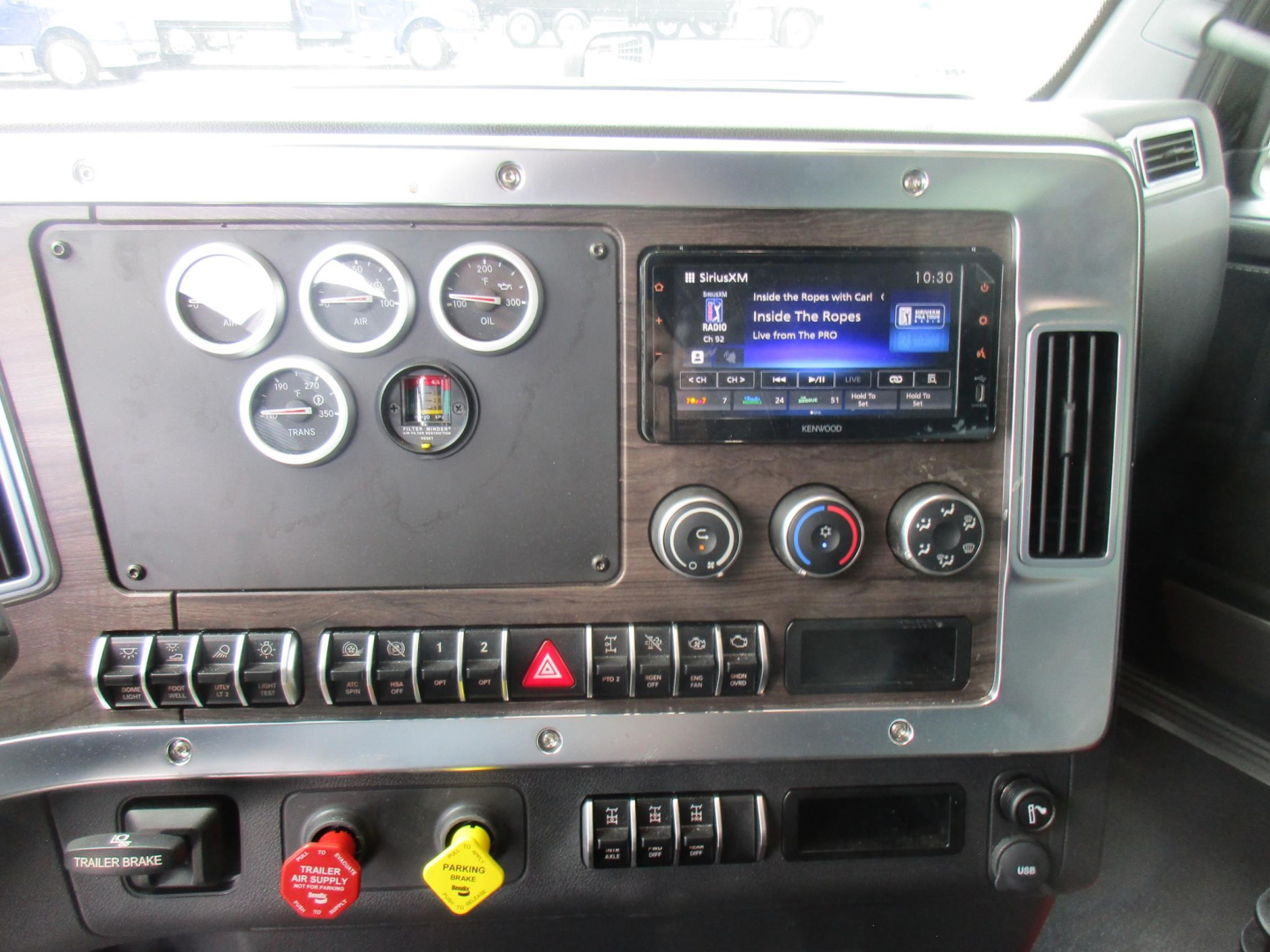 Truck dash panel with multiple gauges and a touchscreen infotainment system. Panel shows round gauges, control switches, hazard button, climate controls, and a woodgrain trim.