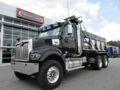 Western Star 47X dump truck in front of Freightliner dealership showing cab, chrome bumper, dual rear wheels, and dump body with ladder rack.