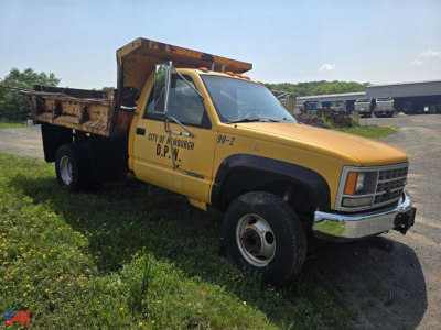 Dump truck showing yellow Chevrolet C/K 3500 Series with dump bed and D.P.N. markings on door and hood; front chrome bumper and black fender trim.