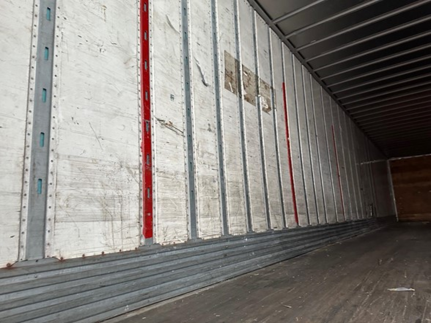 Trailer interior showing metal wall ribs and wooden floor from a 2012 Utility 4000D-X trailer. Visible labels and red and white markings along side.