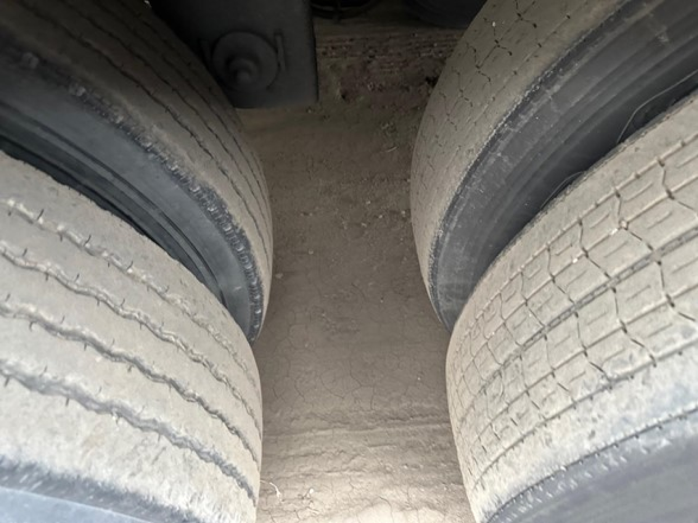 Twin rear trailer wheels showing tread and dirt in-between with a dusty ground