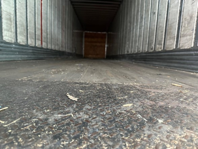Interior view of a trailer bay showing the textured metal floor and metal sidewalls with a wooden rear door at the far end.