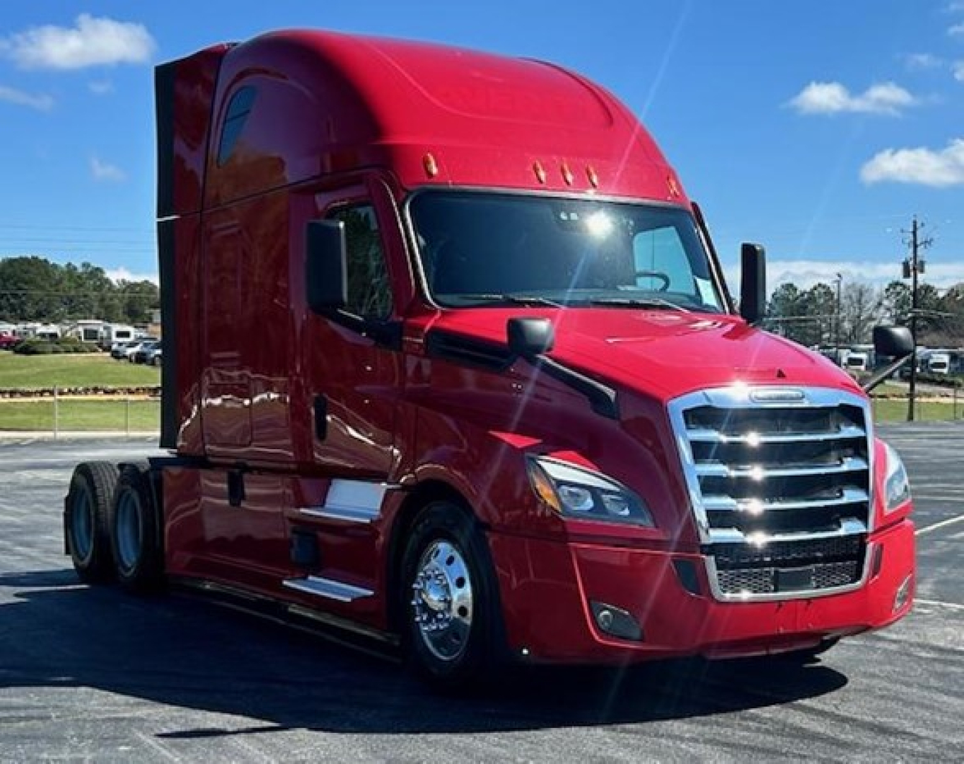 Red Freightliner Cascadia 126 truck in a showroom lot view showing front grille, headlights, and sleeper cab.