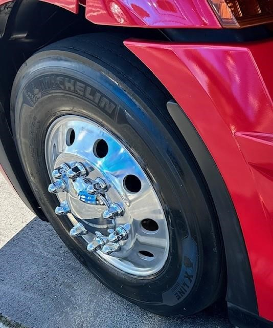 Truck wheel close-up showing Michelin XZE tire and polished chrome dual-stack hub with lug nuts on red Freightliner Cascadia 126 sleeper tractor.