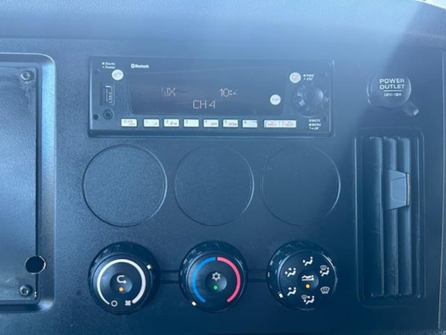 Dashboard controls of a Freightliner Cascadia truck cab showing a radio unit, climate control dials, and cup-holder area.