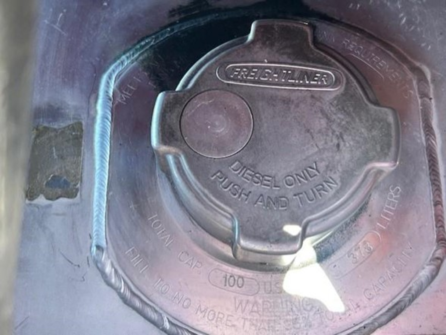 Freightliner fuel cap on diesel tank with 'Diesel Only Push and Turn' label and security ring visible.