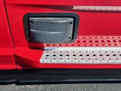 Truck step and fuel cap area on red Freightliner Cascadia 126 showing side step with perforated metal and black trim.