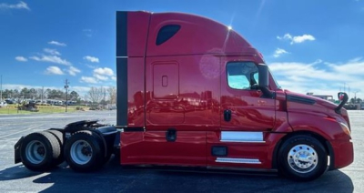 Truck side view of a red 2023 Freightliner Cascadia 126 sleeper cab, featuring tandem rear axles and chrome fuel tanks.