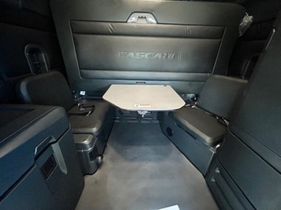 Interior of a Freightliner Cascadia 126 sleeper with table between two seats, black upholstery, rear wall with Cascadia branding.