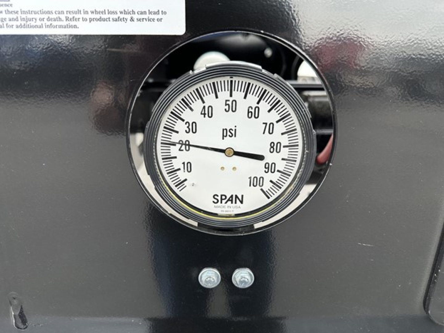 Gauge showing pressure scale 0-100 psi mounted on black trailer side with two small bolts below.