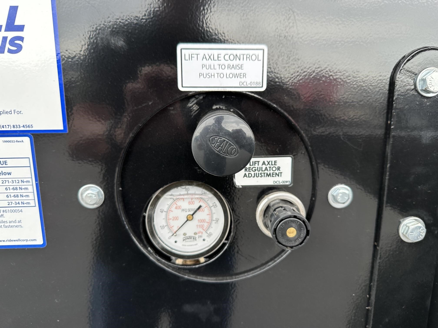 Top view of a Smithco side dump trailer control panel showing lift axle control knob, regulator adjustment label, and a pressure gauge.