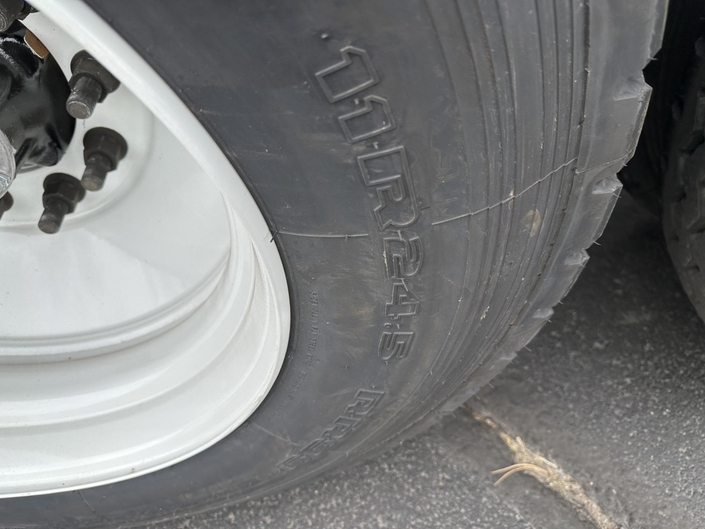 Left wheel and tire of a Smithco side dump trailer showing tire tread and white steel wheel. Visible text on tire: 7.50R16.5 maybe; wheel hub with lug nuts.