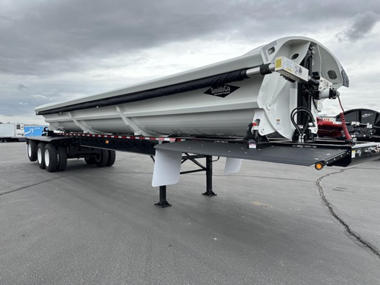 Tri-axle side dump trailer in white with black chassis, SmithCo logo, parked on lot; front end and hydraulic mechanism visible.