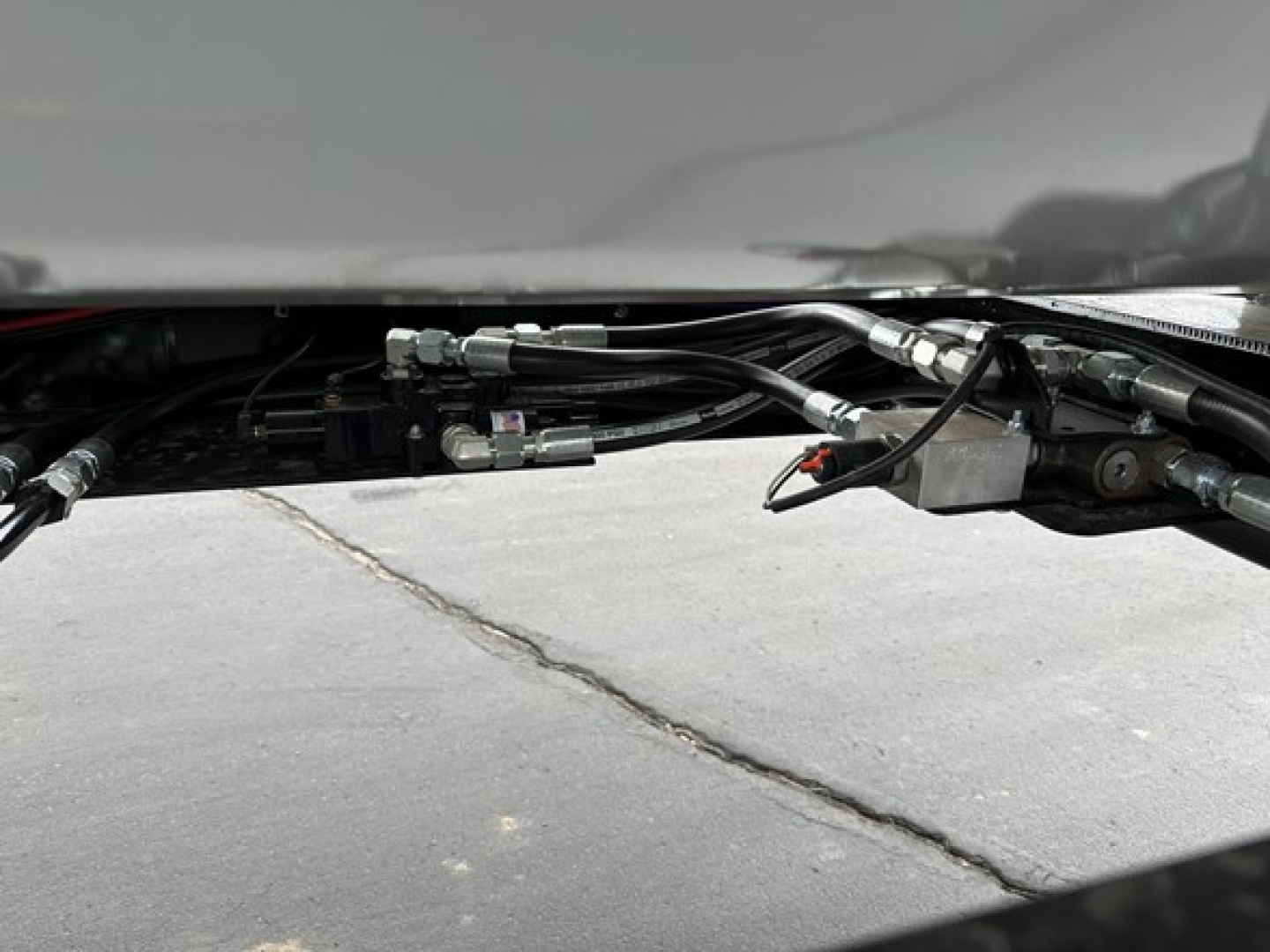 Trailer underside showing hydraulic lines and fittings for a tri-axle side dump trailer.