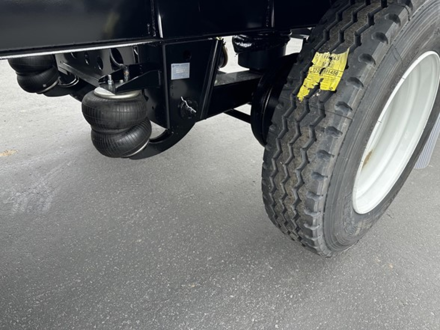 Trailer undercarriage showing air intake canister and suspension near wheel; tire with white rim and yellow safety tag; black frame of a Smithco tri-axle side dump.
