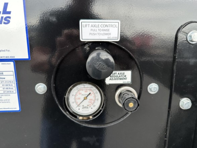Panel view of a Smithco side dump trailer showing lift actuator control label, dial gauge, and adjustment knob with surrounding bolts.