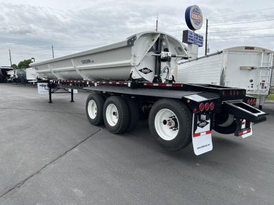 Trailer side view showing a Smithco side dump W super spread, tri-axle with white wheels and gray hopper, rear mud flaps and reflective tape.