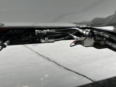 Trailer undercarriage showing hydraulic lines and fittings with metal reservoir and hoses.