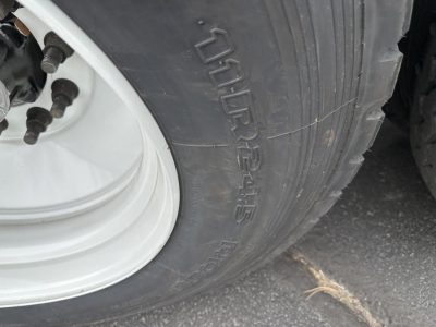 Left wheel and tire of a Smithco side dump trailer showing tire tread and white steel wheel. Visible text on tire: 7.50R16.5 maybe; wheel hub with lug nuts.