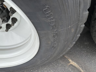 Tire sidewall on a trailer with a white wheel rim visible; part of a large tire showing 'GAL? ‘' and leafs of the wheel hub; portion of trailer body tire label area.
