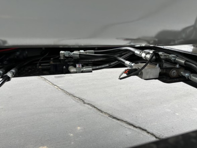 Trailer underside showing hydraulic lines and fittings for a tri-axle side dump trailer.