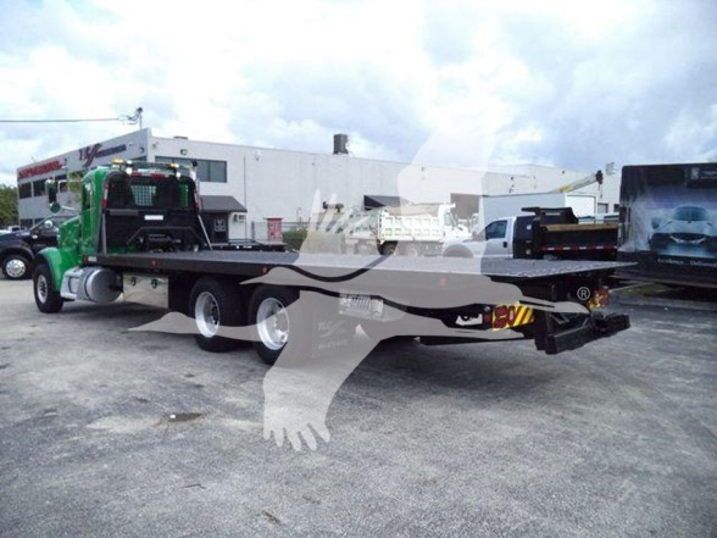 2014 Peterbilt 367 rollback truck with a flatbed, showing VIN sticker area and equipment behind; venue lot with other trucks in background.