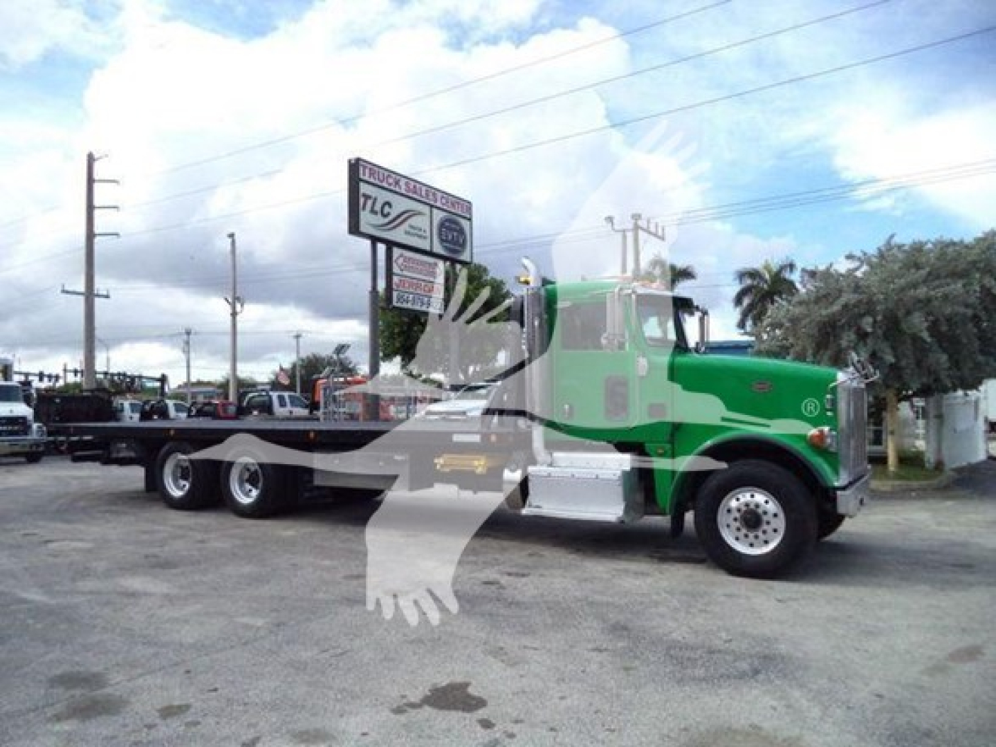 Peterbilt 367 rollback truck side view showing green and silver cab, long flatbed, dual rear axles, and front wheels; truck is in outdoor lot.