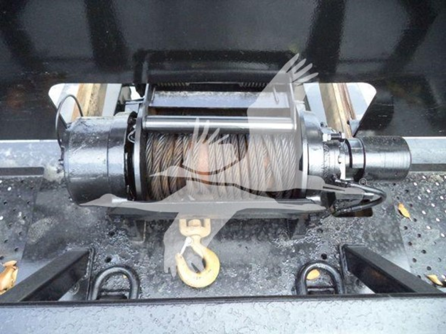Winch mechanism with steel drum and hook, mounted on a trailer hitch frame, visible hydraulic lines and metal rollers.