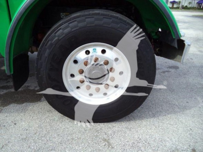 Truck wheel assembly showing front axle with large black tire and white polished hubcap, green fender in background.