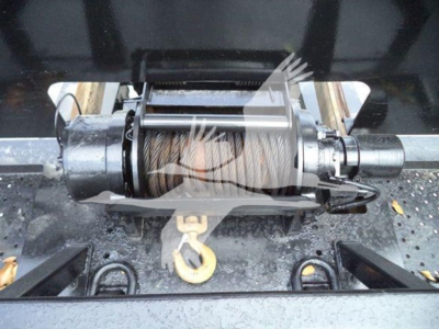 Winch mechanism with steel drum and hook, mounted on a trailer hitch frame, visible hydraulic lines and metal rollers.