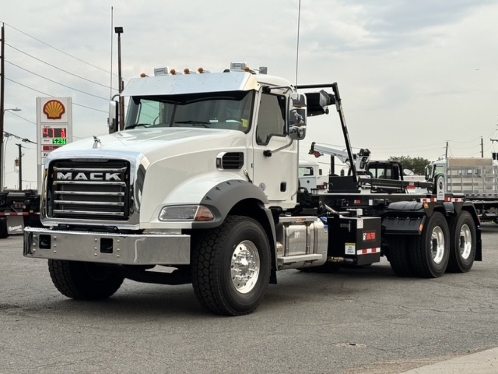 Front-left view of a white 2027 Mack GR64B roll-off truck showing Mack grille and chassis with hook lift equipment.