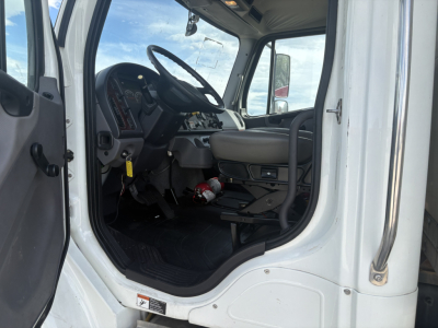 Freightliner M2-106 truck cab interior showing steering wheel, dashboard, pedals, and seats from open driver door.
