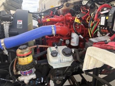 Freightliner M2-106 engine bay showing blue radiator hose, red engine, white coolant reservoir, and various hoses and filters.