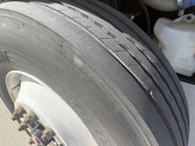 Freightliner M2-106 front tire and wheel well showing tire treads and nearby reservoir and hoses.