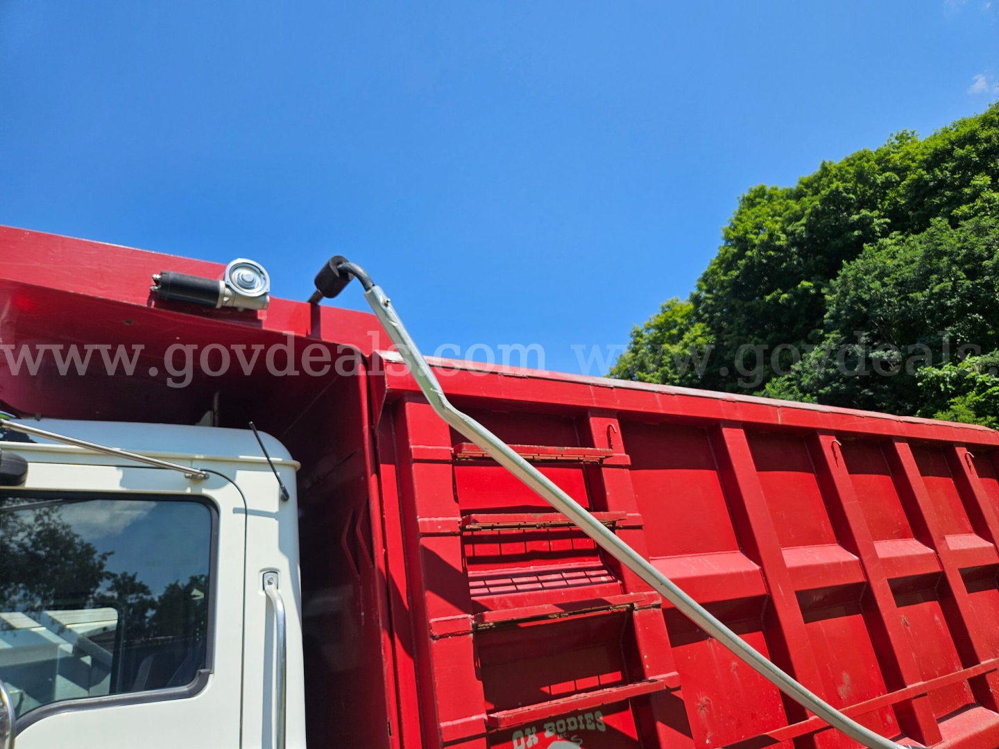 Mack CV713 dump truck cab and red dump body with watermarked background and blue sky