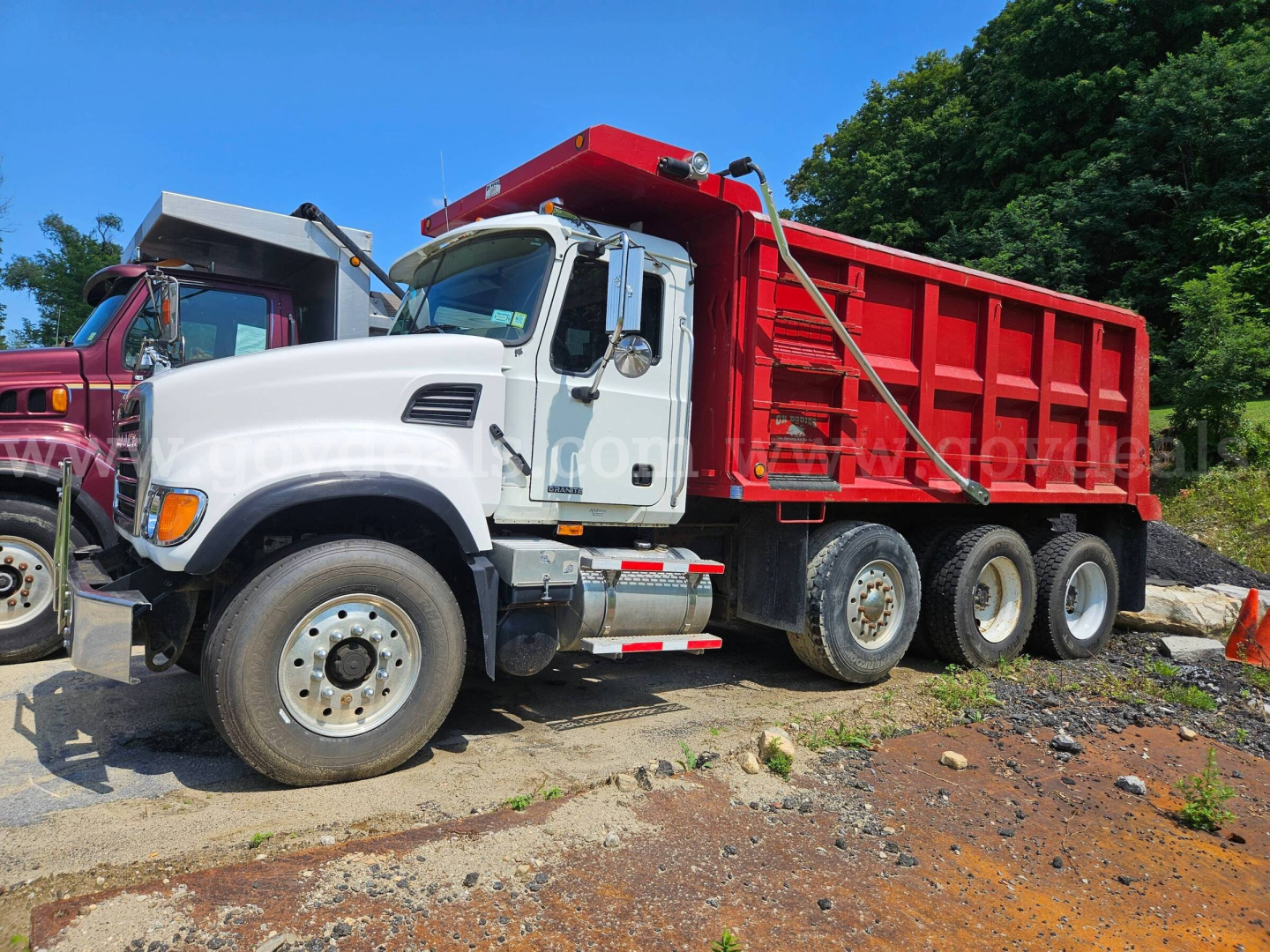 Mack CV713 dump truck with white cab and red dump body's side view showing dual rear axles.