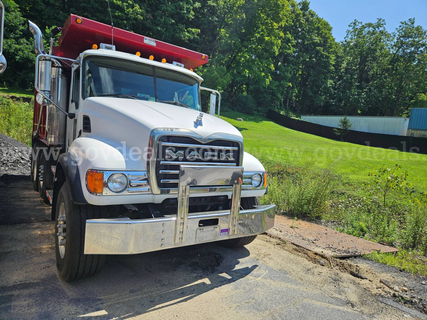 Mack CV713 dump truck front view showing white cab and chrome bumper with red dump bed edge.