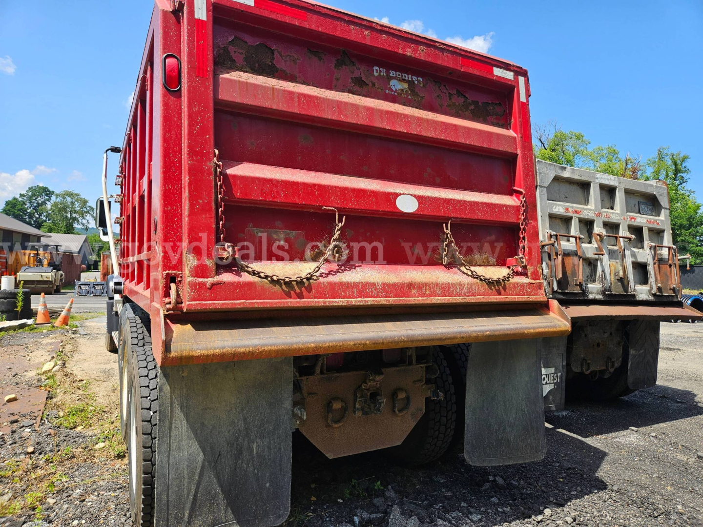 Rear view of a red 2007 Mack CV713 dump truck showing dump bed tailgate, chains, mud flaps, and dual rear wheels.