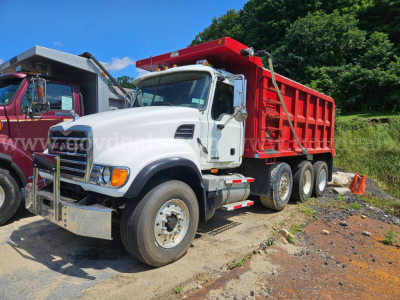 Dump truck cab and red dump bed with Mack CV713 model tag, front chrome bumper, dual rear axles, stock number 32136-70, white cab, on dirt lot.