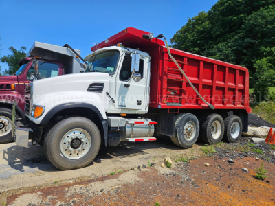 Mack CV713 dump truck with white cab and red dump body's side view showing dual rear axles.