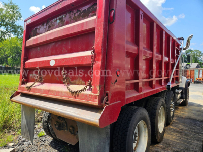 Dump truck rear view showing red bed, chains, and dual rear axles on a Mack CV713.