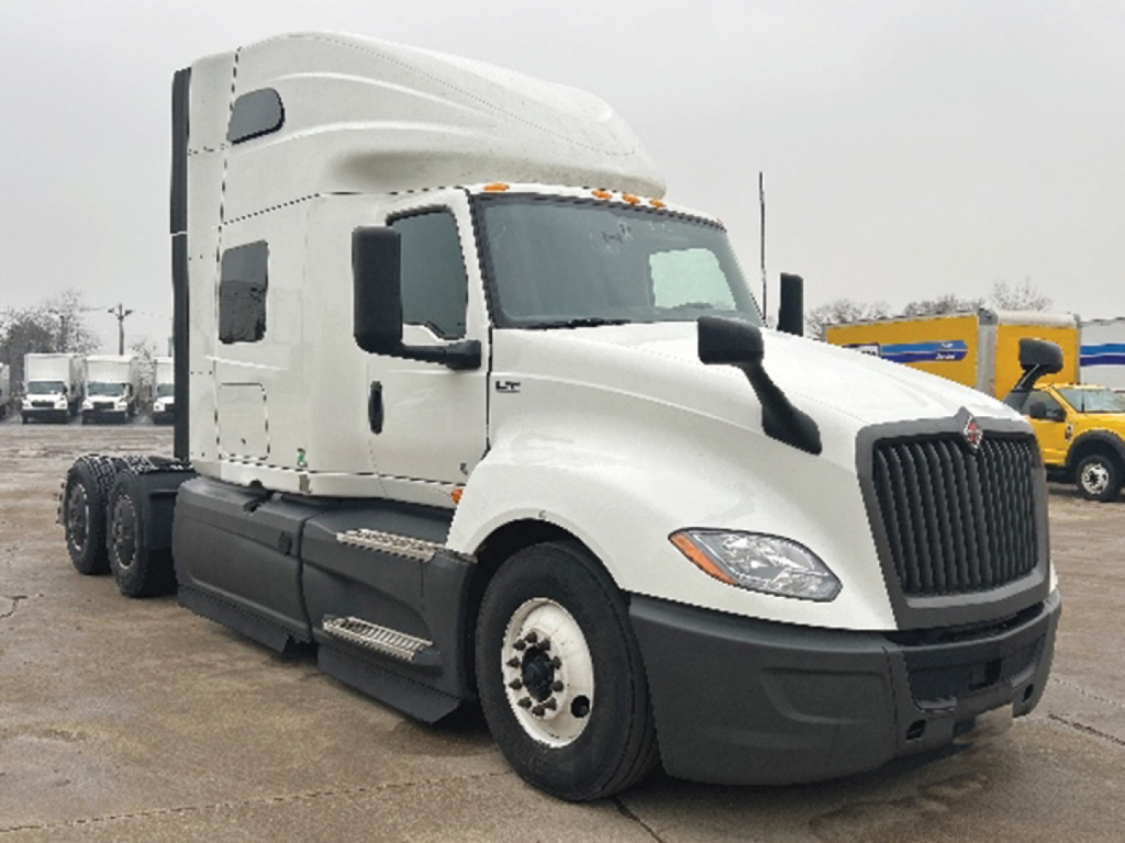 Truck shows 2023 International LT625 conventional sleeper in white, side view with twin rear axles, large grille, and fuel tanks visible.