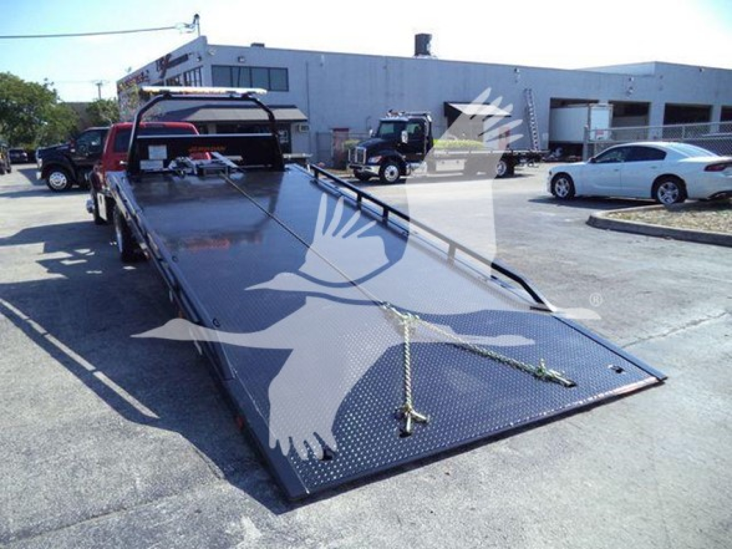 Ram 5500 rollback flatbed tow truck in a dealership lot with extended metal deck and winch anchor points visible.